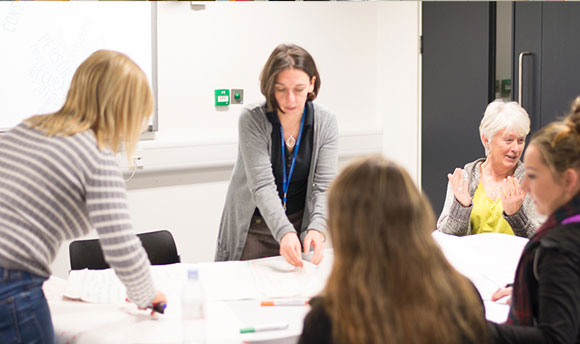 A group of Queen Margaret University Students and lecturer chatting around a table